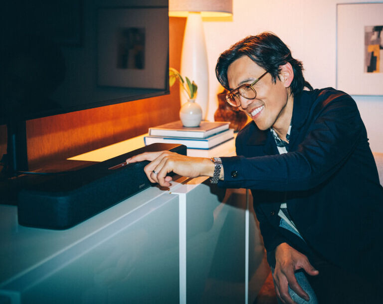 Man interacting with the touch controls on a Denon Wireless sound bar.
