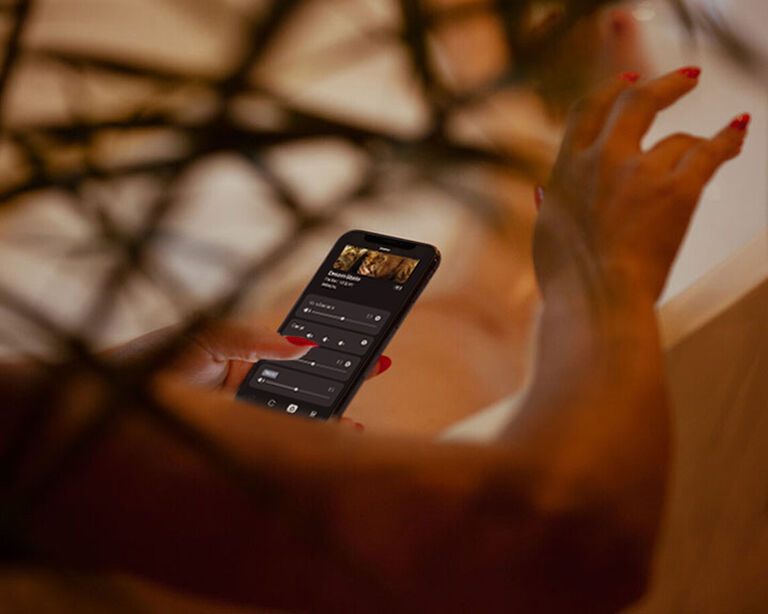 Person using the HEOS® app on their mobile phone to control the volume on their multi-room audio system